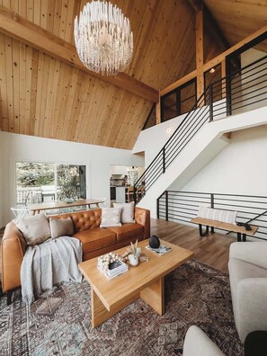A modern living room with a wooden ceiling, a staircase, and a view of the outdoors. - The Lakeview House (w/ hot tub, by @To_Dwell_Here) (Lake Arrowhead)