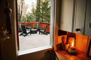Vista a través de una ventana que muestra un balcón exterior con sillas y una mesa, un armario de madera con un farol en su interior, y un marco de puerta.