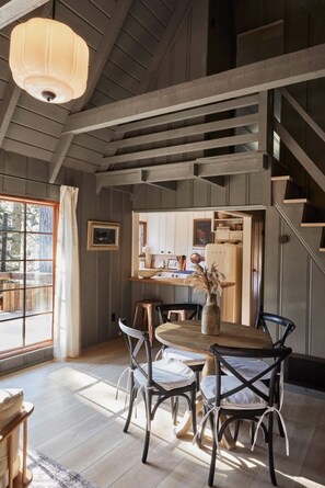 Un comedor con una mesa y sillas de madera, una lámpara colgante, y vistas de la cocina y la escalera.