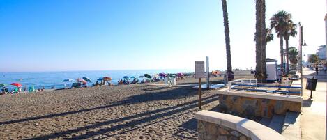 A beach with umbrellas, palm trees, and a stone wall.