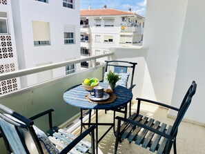 En balkon med et rundt bord, stole, en skål med frugt, en potteplante og en dekorativ væg.