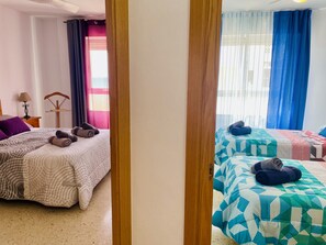 Et hotelværelse med to senge, en stol, en lampe og et vindue med gardiner.