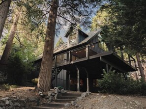 A rustic cabin with a wooden deck, surrounded by tall trees. - Ravenwood House, lakefront on Orchard Bay (Lake Arrowhead)