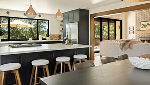 A modern kitchen with a central island, bar stools, pendant lighting, and a view of the outdoors. - Geneva Pines (walk to lake!) (Lake Arrowhead)