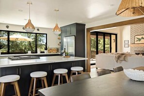 Une cuisine moderne dotée d’un îlot central, de tabourets de bar, de luminaires suspendus et offrant une vue sur l’extérieur.