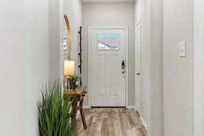 Un pasillo con una puerta blanca, una consola de madera con una lámpara y un espejo.