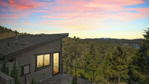 A modern house with a large window, a balcony, and a view of a forested landscape.