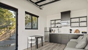 A modern kitchen with a dining area, a sofa, and a view of a staircase leading outside.