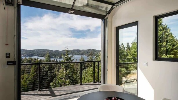 A modern room with a large glass door leading to a balcony overlooking a lake and forest.