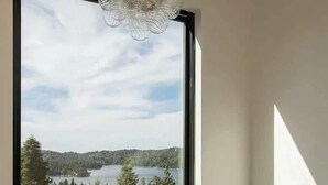 A modern bathroom with a freestanding bathtub, a large window with a view of a lake and forest, and a unique chandelier.