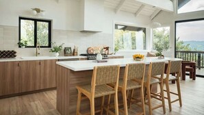 Uma cozinha moderna com uma ilha grande, banquetas de madeira e vista para o exterior.