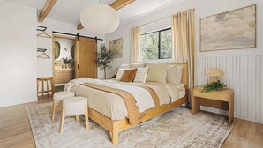 Quarto com cama de madeira, mesa de cabeceira, luminária pendente, janela com cortinas e radiador.
