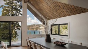 En matplats med ett långt bord, stolar, en vas och utsikt över en sjö och träd.