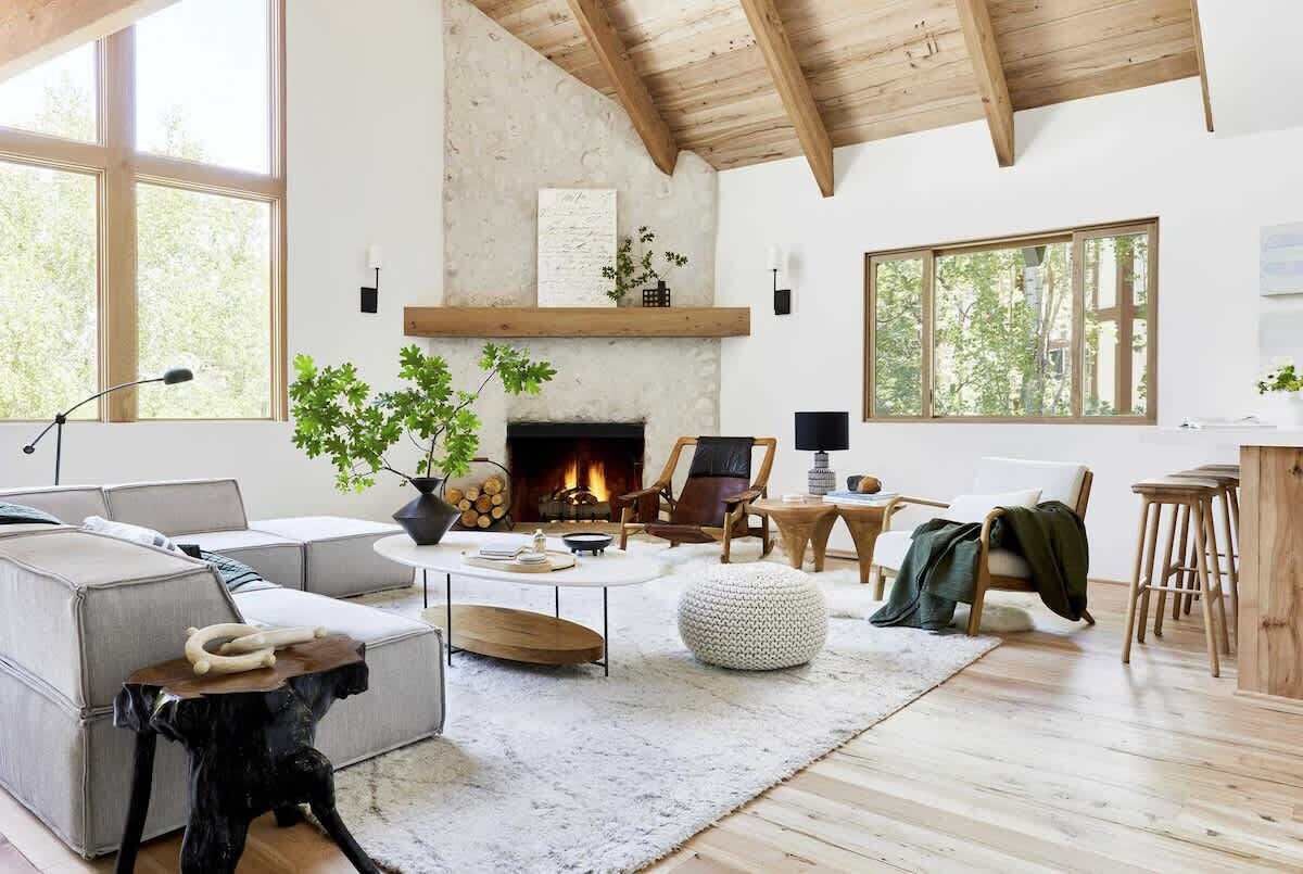 A spacious living room with a fireplace, large windows, and a high ceiling.