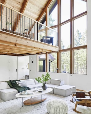 A spacious living area with a high ceiling, large windows, a built-in loft, and a cozy seating arrangement. - The Mountain House, by designer Emily Henderson (Lake Arrowhead)