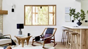 Ein geräumiges Wohnzimmer mit hoher Decke, einem großen Fenster, einem hölzernen Schaukelstuhl, einer Bar und einem gemütlichen Kamin.