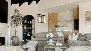 Ein Wohnzimmer mit Kamin, Sofas, einem Couchtisch und einer dahinterliegenden Küchenzeile.