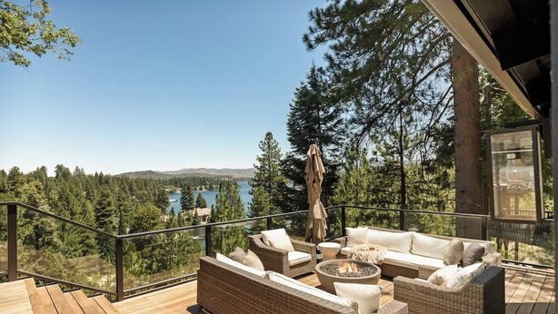 Eine Terrasse mit Korbmöbeln, einer Feuerstelle und Blick auf See und Wald.