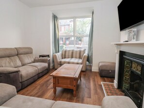 A living room with a sofa, armchairs, a coffee table, a fireplace, and a television. - 93 Abbotsbury Road (Weymouth)