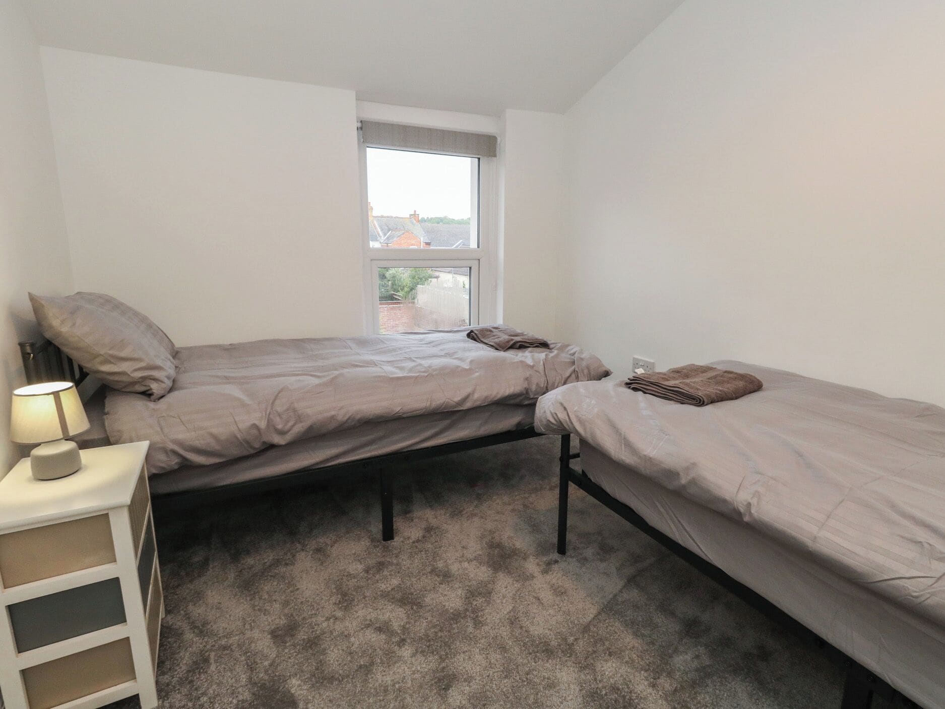 Une petite chambre avec un seul lit, deux lits, une table de chevet et une fenêtre.