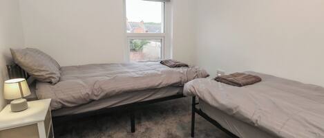 Une petite chambre avec un seul lit, deux lits, une table de chevet et une fenêtre.