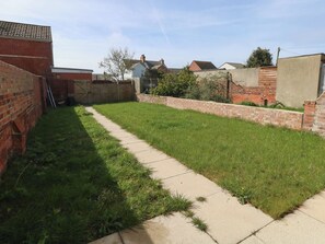 A backyard with a paved walkway, a brick wall, and a grassy area. - 93 Abbotsbury Road (Weymouth)