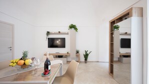 Et moderne spiseområde med et bord dækket til to personer, et vægmonteret fladskærms-tv og krukkeplanter.