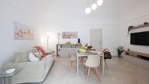 En moderne stue med sofa, spisebord, stole, fjernsyn og kunst på væggene.
