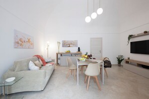 A modern living room with a sofa, dining table, chairs, a TV, and artwork on the walls. - CENTRALISSIMO APPARTAMENTO COMPLETAMENTE RISTRUTTURATO NEL CUORE DI AMALFI (Amalfi)