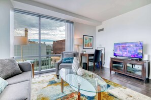Ein modernes Wohnzimmer mit einer Couch, einem Glastisch, einem Fernseher und einem großen Fenster mit Blick auf die Stadt.