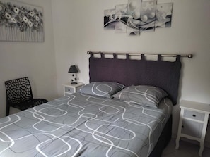 Ein Schlafzimmer mit Bett, Nachttisch, Stuhl und Wandbild.