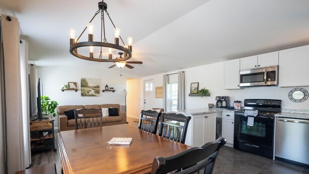 A modern kitchen with a dining area, featuring a wooden table, chairs, a chandelier, and built-in appliances. - Peaceful Ozark Escape Near the Artesian Well, 2BR/2BA Retreat (Marquand)