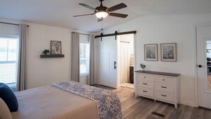 A bedroom with a bed, a ceiling fan, a dresser, and a door leading to a bathroom. - Peaceful Ozark Escape Near the Artesian Well, 2BR/2BA Retreat (Marquand)