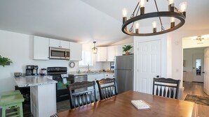 A modern kitchen with white cabinets, stainless steel appliances, and a wooden dining table. - Peaceful Ozark Escape Near the Artesian Well, 2BR/2BA Retreat (Marquand)