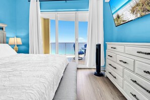 A bedroom with a bed, a dresser, a TV, and a balcony with a view of the beach. - 🦞Gulf Front | Beach Service | Pool | 2BR Ocean Villa 2101🌅 (Panama City Beach)