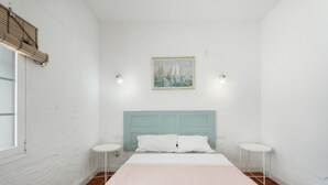 A bedroom with a bed, two bedside tables, a headboard, a window with blinds, and a painting on the wall.