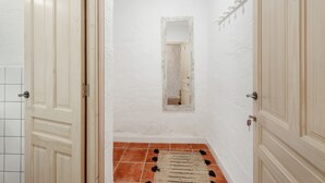 A hallway with white walls, a tiled floor, and a mirror on the wall.