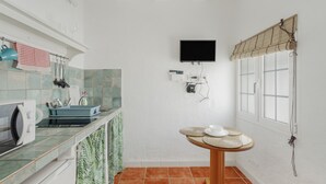 A compact kitchen with a microwave, sink, and a small table with a cup and saucer.