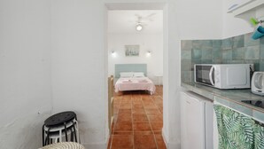 A narrow hallway leading to a bedroom with a bed, a ceiling fan, and a wall-mounted light.