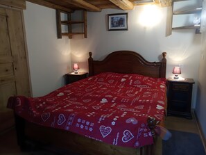 Un dormitorio con una cama de madera, dos mesitas de noche con lámparas, un armario de madera, un cuadro en la pared y una colcha de cama roja con estampado.