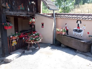 Um edifício rústico com fachada de madeira, um mural de uma vaca e uma pessoa, e cestos com flores pendurados.