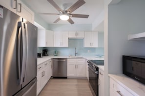 Eine moderne Küche mit Edelstahl-Kühlschrank, Geschirrspüler und Backofen, weißen Schränken, einem Deckenventilator und einer gefliesten Spritzschutzwand.