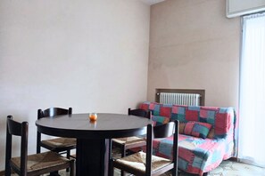 Ein Zimmer mit einem runden Tisch, vier Stühlen, einem farbenfrohen Sofa und einem Heizkörper.