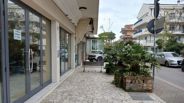 A stone-tiled sidewalk leading to a building with large glass doors and a bench. - RG019 - Bellaria, bright three-room apartment 100 meters from the sea (Bellaria-Igea Marina)