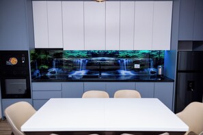 A modern kitchen with a waterfall display, a built-in oven, and a dining area with chairs. - Modern 110 sqm apartment near Tirana and airport (Valias)