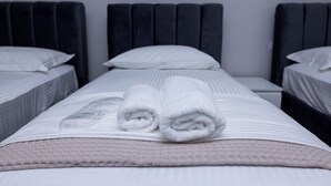 A hotel room with two beds, each with a dark headboard, white bedding, and rolled white towels on the beds. - Modern 110 sqm apartment near Tirana and airport (Valias)