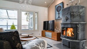 Ein modernes Wohnzimmer mit Kamin, Fernseher und Blick ins Grüne.