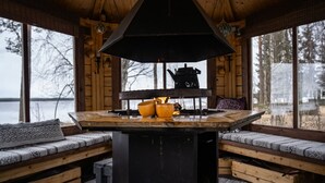 Ein Interieur einer Holzhütte mit einem Tisch in der Mitte, hölzernen Bänken und Blick auf einen See.
