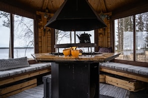 Interior d'una cabana amb taula central, seients de fusta i vista d'un llac.
