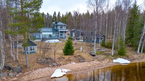 Eine Blockhütte am Seeufer mit einer großen Terrasse, einer Veranda und einem kleinen Boot, das am Wasser liegt.